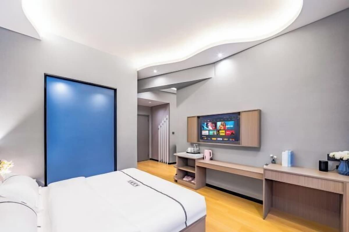 A modern bedroom with a bed, a TV mounted on the wall, and a desk with a chair.