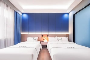 A modern hotel room with two beds, a nightstand, and a wall-mounted light fixture. - Golden Dragon Hotel (Red River Maitreya Branch) (Mile)