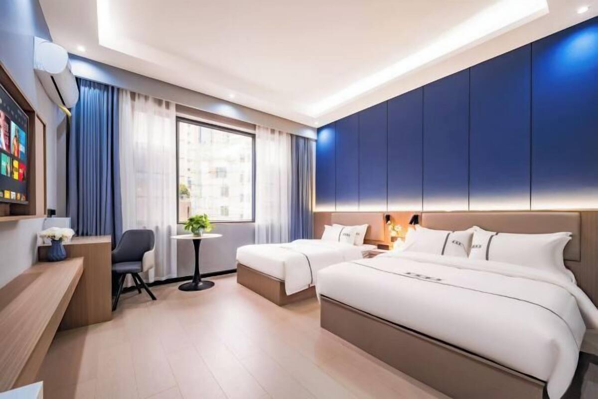 Ein modernes Hotelzimmer mit einem großen Bett, einem Schreibtisch, einem Sessel und einem kleinen Tisch mit einer Pflanze.