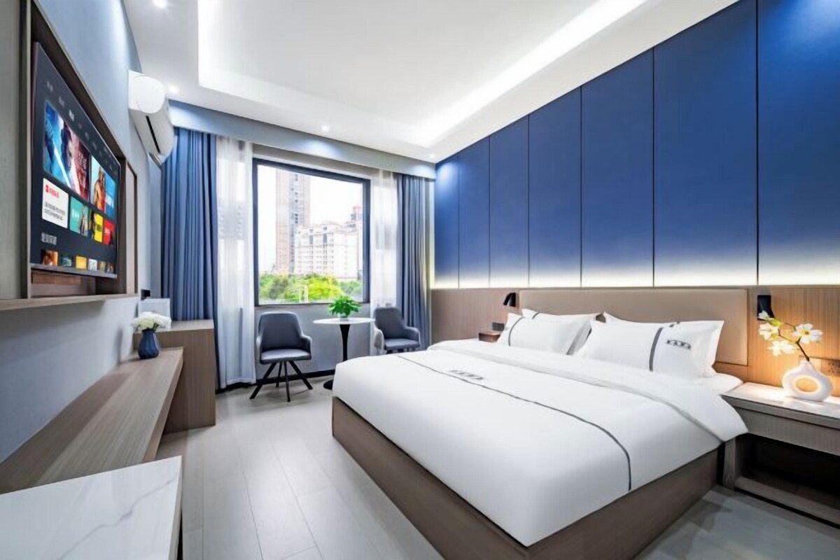 A modern hotel room with a large bed, a desk, a chair, and a small table.