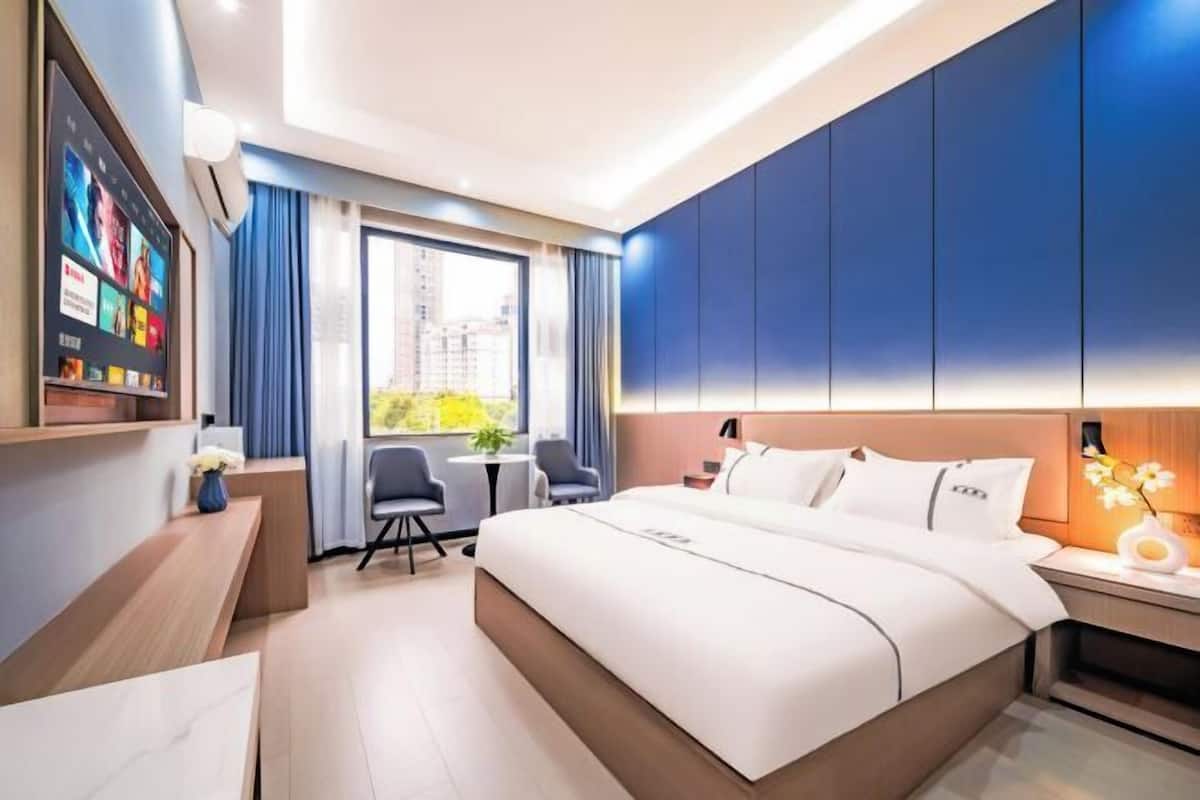 Ein modernes Hotelzimmer mit einem großen Bett, einem Schreibtisch, einem Stuhl und einem an der Wand befestigten Fernseher.
