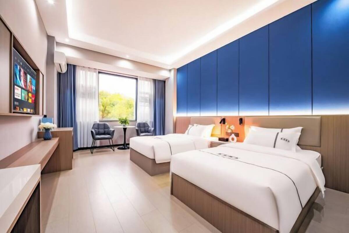 Ein Hotelzimmer mit zwei Betten, einem Schreibtisch, einem Sessel und einem Fernseher.