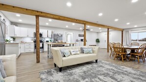 A spacious living area with a sofa, a dining table with chairs, a kitchen in the background, and wooden beams on the ceiling.