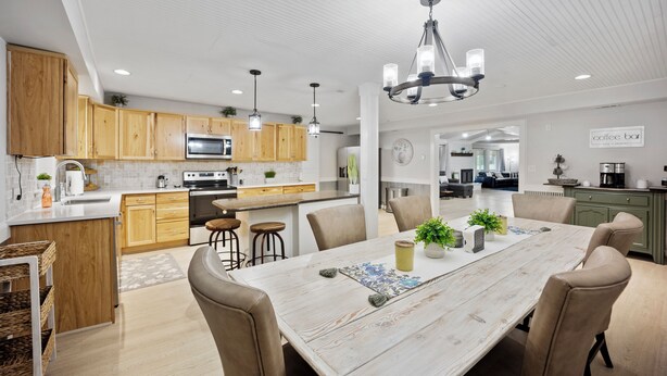 A modern kitchen with wooden cabinets, a central island, and a dining area with a large table and chairs.