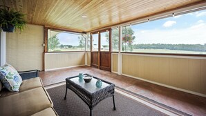 A room with a wooden ceiling, a cushioned bench, a wicker table, and a view of the outdoors.
