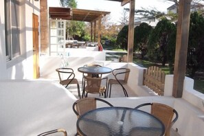 An outdoor patio with round tables and wicker chairs, a pergola, and a view of a garden and pool. - Sheep Chimney (Hualien)