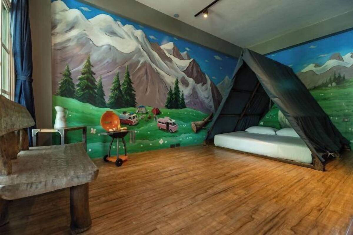 Una habitación con un mural de montañas, una cama tipo tienda, una silla de madera y una pequeña mesa con una lámpara.