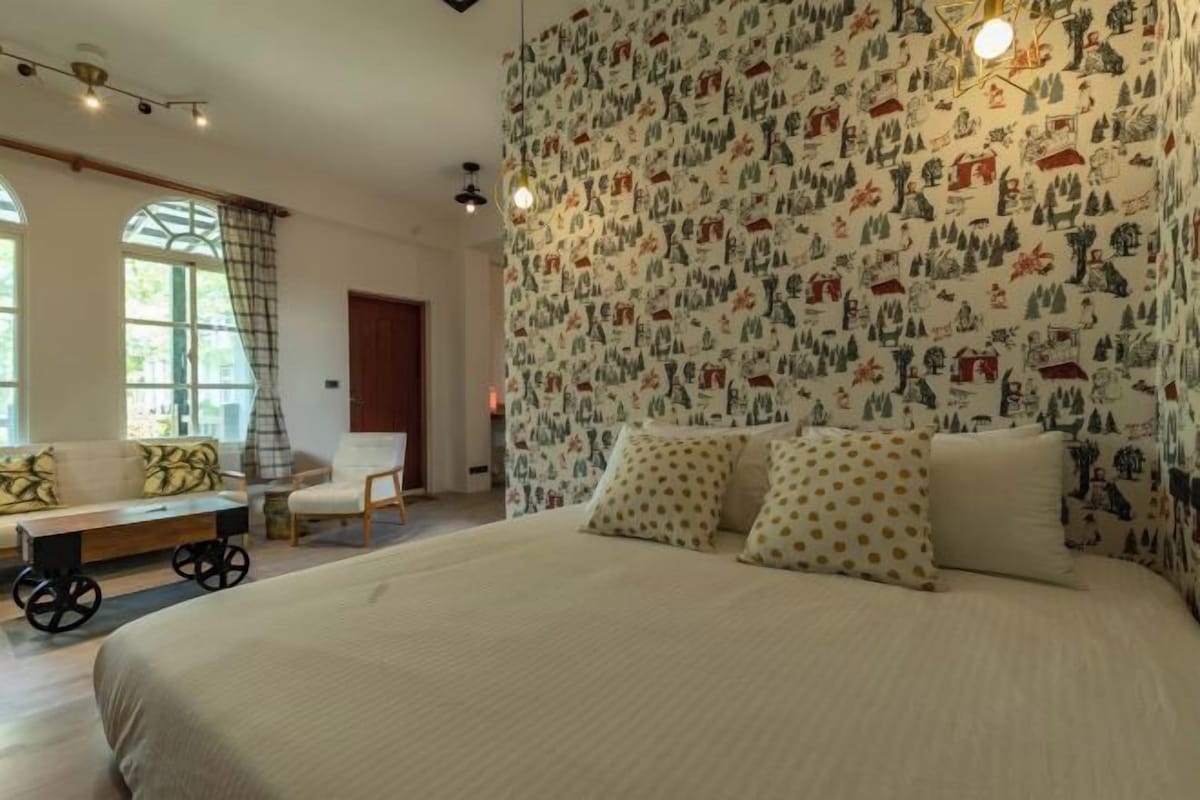 A bedroom with a large bed, a sofa, a small table, and a patterned wallpaper.