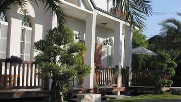 A white building with a covered porch, a small tree, and a concrete planter.