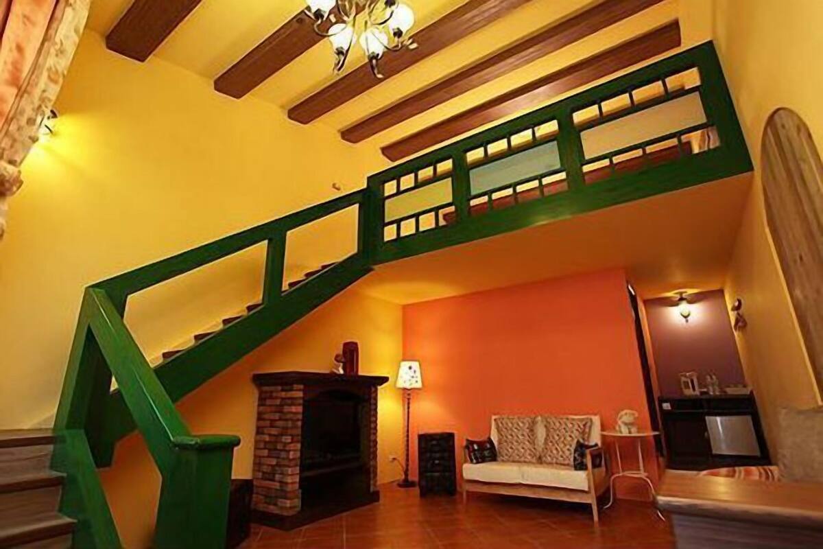 Una escalera con barandas verdes, una chimenea, un sofá y una lámpara en una habitación con paredes anaranjadas.