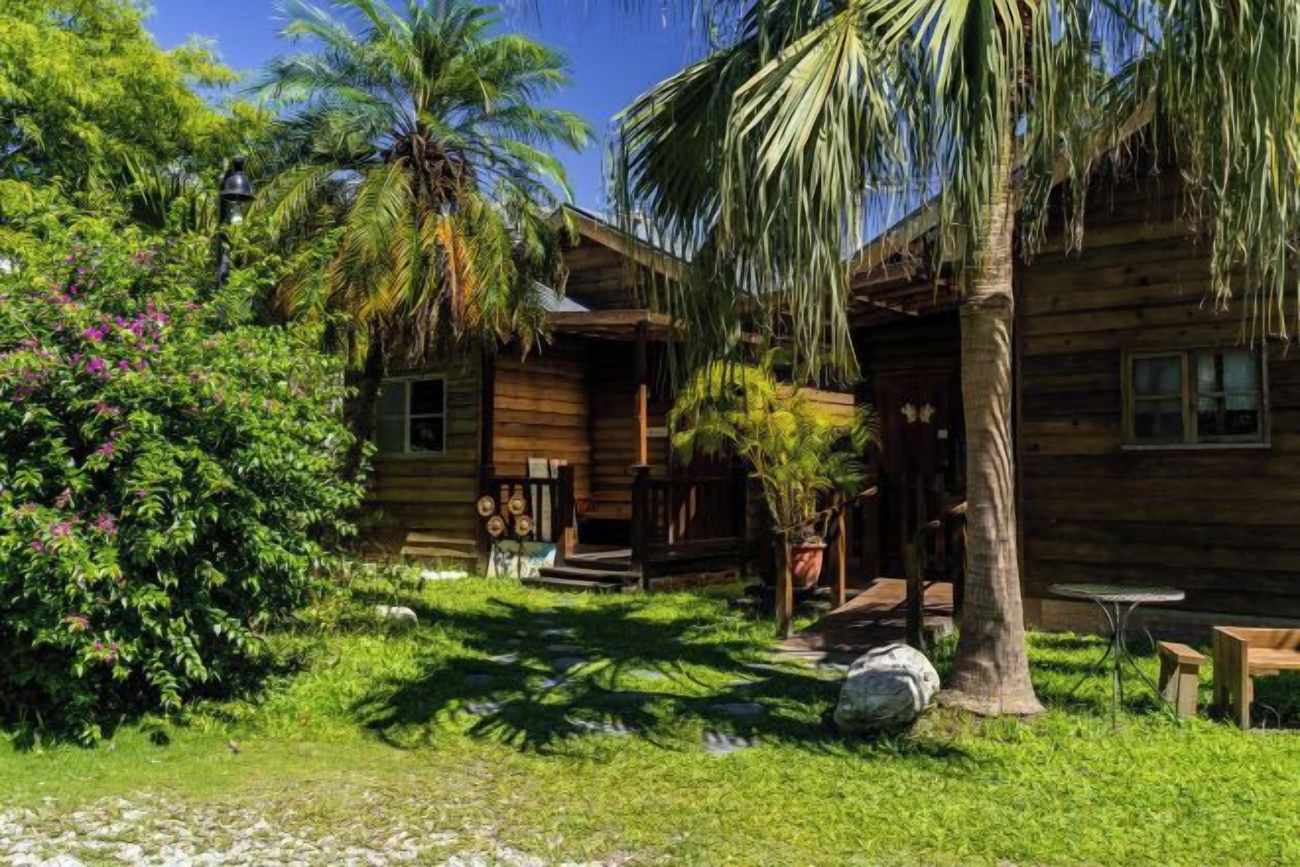 Uma cabana de madeira com varanda, rodeada por vegetação exuberante e palmeiras.