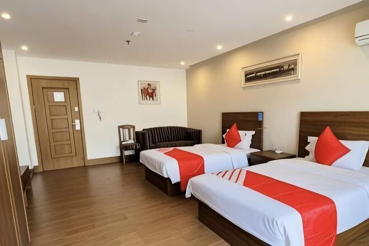 A hotel room with two beds, a wooden floor, a door, a nightstand, and a wall-mounted artwork.
