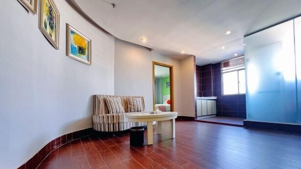 A spacious room with a curved wooden floor, a sofa, a small table, and framed artwork on the wall. - HaoJiang Hotel (Huizhou)