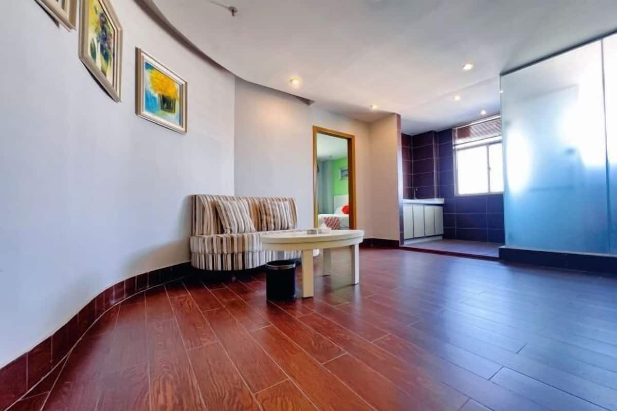 A spacious room with a curved wooden floor, a sofa, a small table, and framed artwork on the wall.