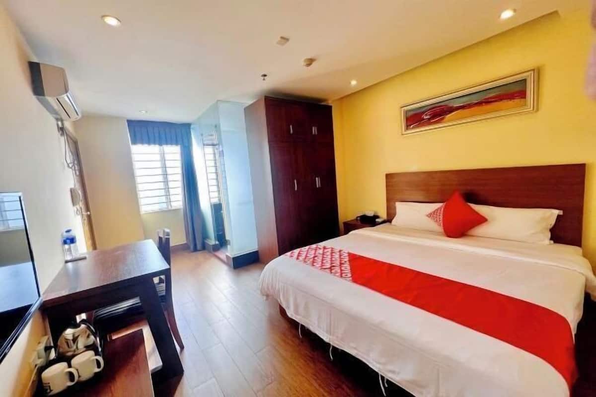 A hotel room with a large bed, a desk with a chair, a TV, and a wardrobe.