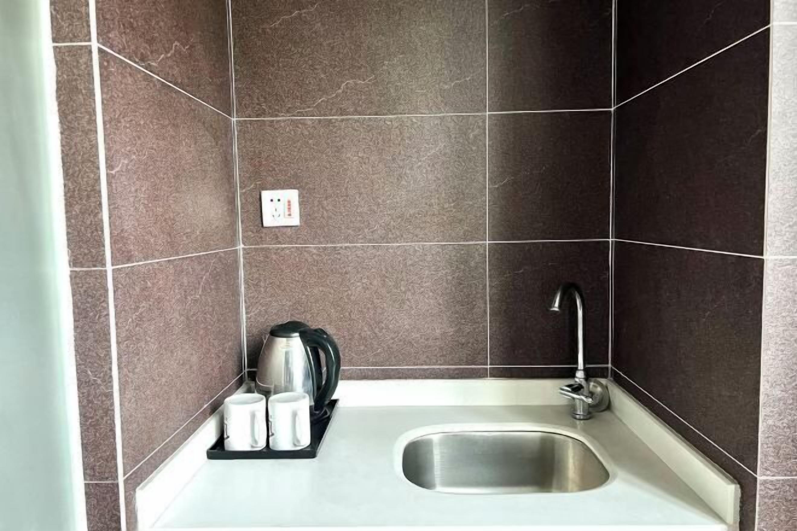 A small kitchen area with a sink, a kettle, and two cups on a tray.