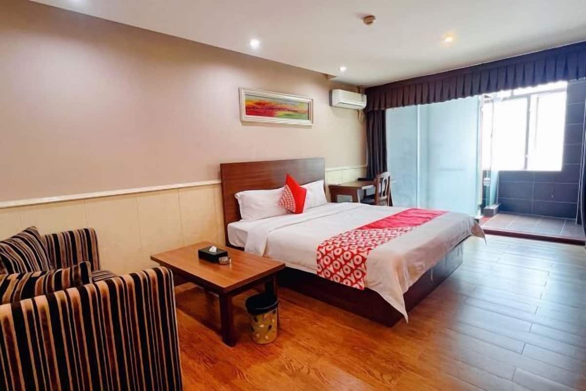 A hotel room with a bed, a small table, a chair, a sofa, and a window with a view.