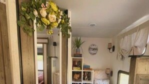 Ein schmaler Flur, der zu einem Schlafzimmer mit Bett, Bücherregal und kleinem Fenster führt.