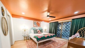 Un dormitorio con cama, mesitas de noche, una silla, ventana con cortinas y ventilador de techo.