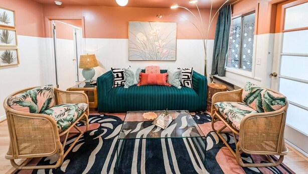 Una sala de estar acogedora con un sofá color turquesa, dos sillones de mimbre, una mesa de centro de vidrio y una alfombra estampada de cebra.