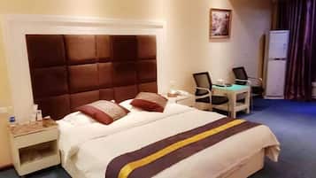 A hotel room with a large bed, a desk, a chair, and a refrigerator.