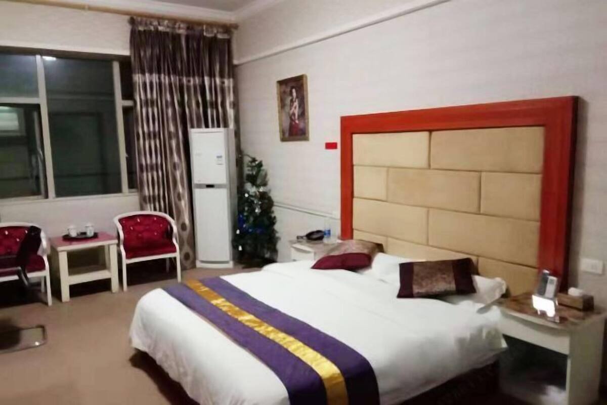 Habitación de hotel con una cama grande, un escritorio pequeño, dos sillas, una mesita de noche y una ventana con cortinas.
