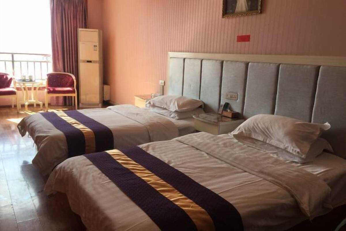 Habitación de hotel con dos camas, una mesita con sillas, un armario y una ventana con cortinas.
