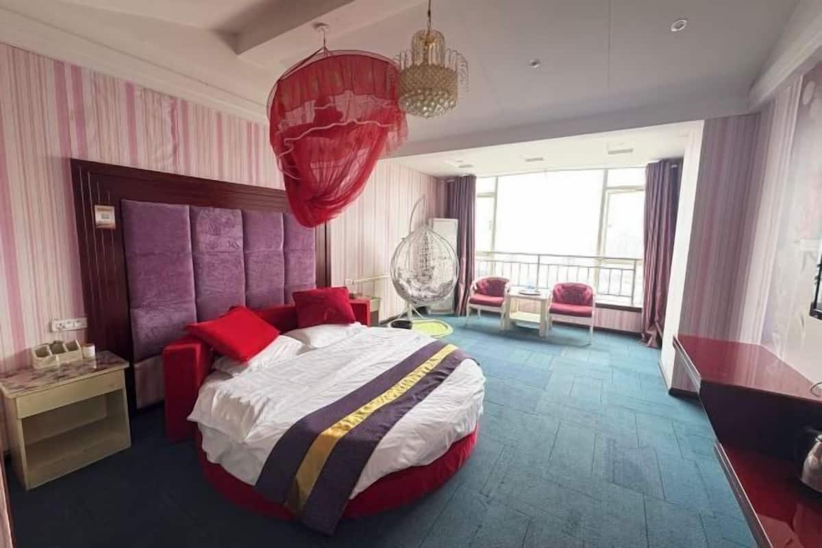 A hotel room with a large bed, a bedside table, a chair, a hanging chair, and a balcony with a view.