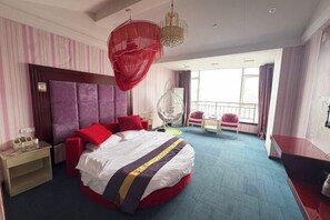 Habitación de hotel con una cama grande, una mesita de noche, una silla, un sillón colgante y un balcón con vistas.