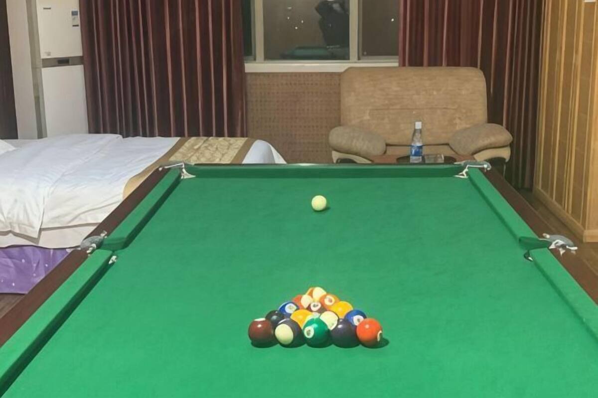 Una mesa de billar con bolas, un sofá, una silla y una ventana con cortinas.