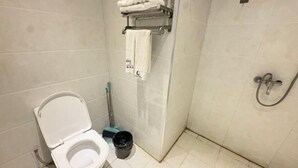 Une salle de bain équipée de toilettes, d’une douche, d’un porte-serviettes et d’un balai.