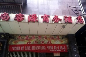 Un letrero de hotel con letras rojas y blancas, un cartel con caracteres chinos, y parte de la fachada de un edificio.
