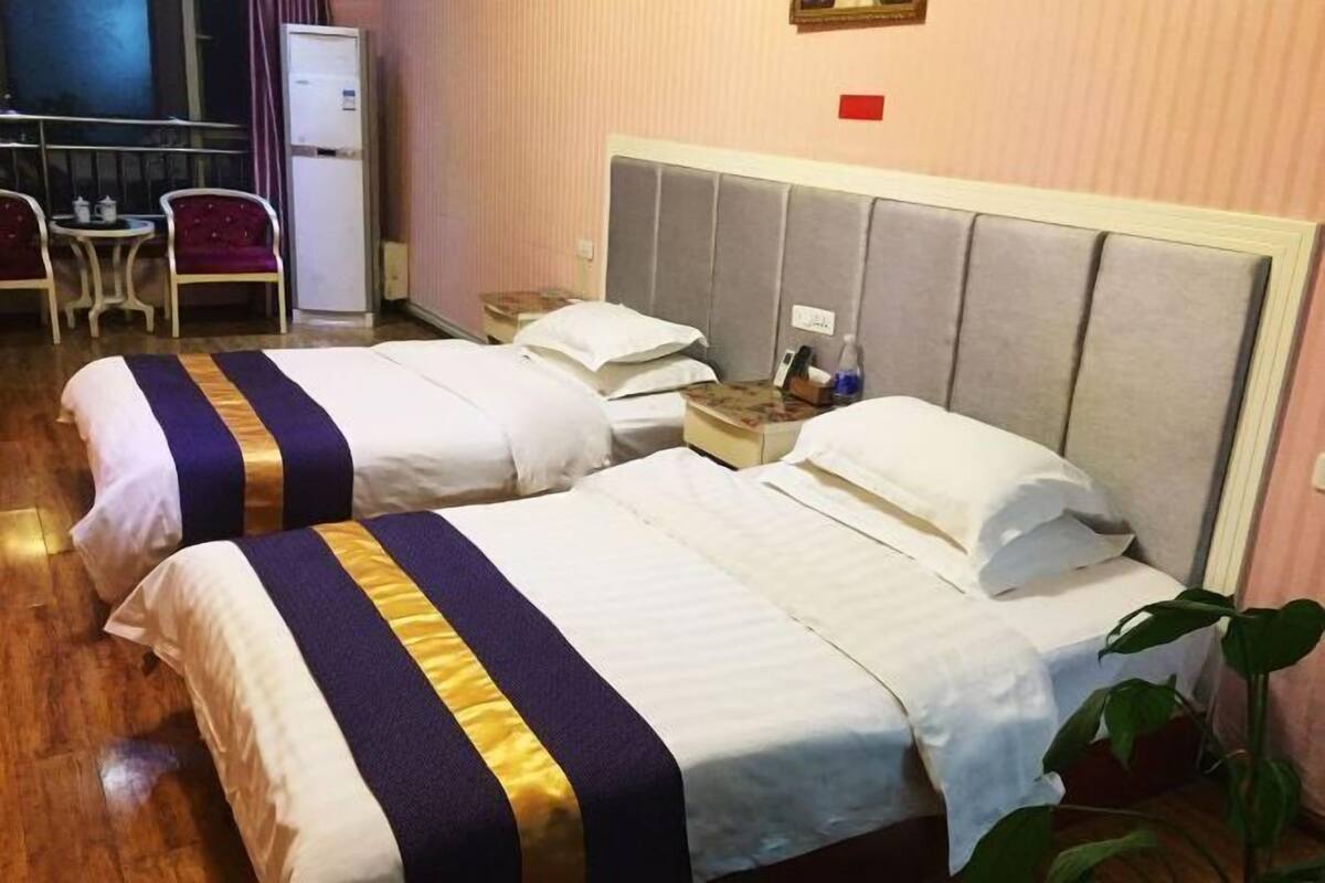 Habitación de hotel con dos camas, una mesita con una silla, un refrigerador y una planta.