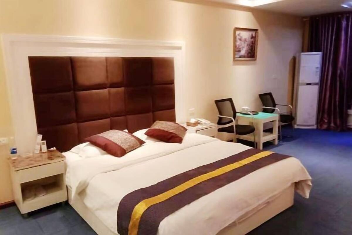 Habitación de hotel con una cama grande, un escritorio con silla, una mesita de noche y un refrigerador.
