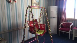 Une pièce avec un papier peint à rayures, une chaise suspendue rouge et blanche, une chaise rouge, une table blanche et un tableau encadré accroché au mur.