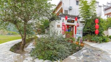 Edificio tradicional con un letrero, rodeado de follaje y senderos de piedra.