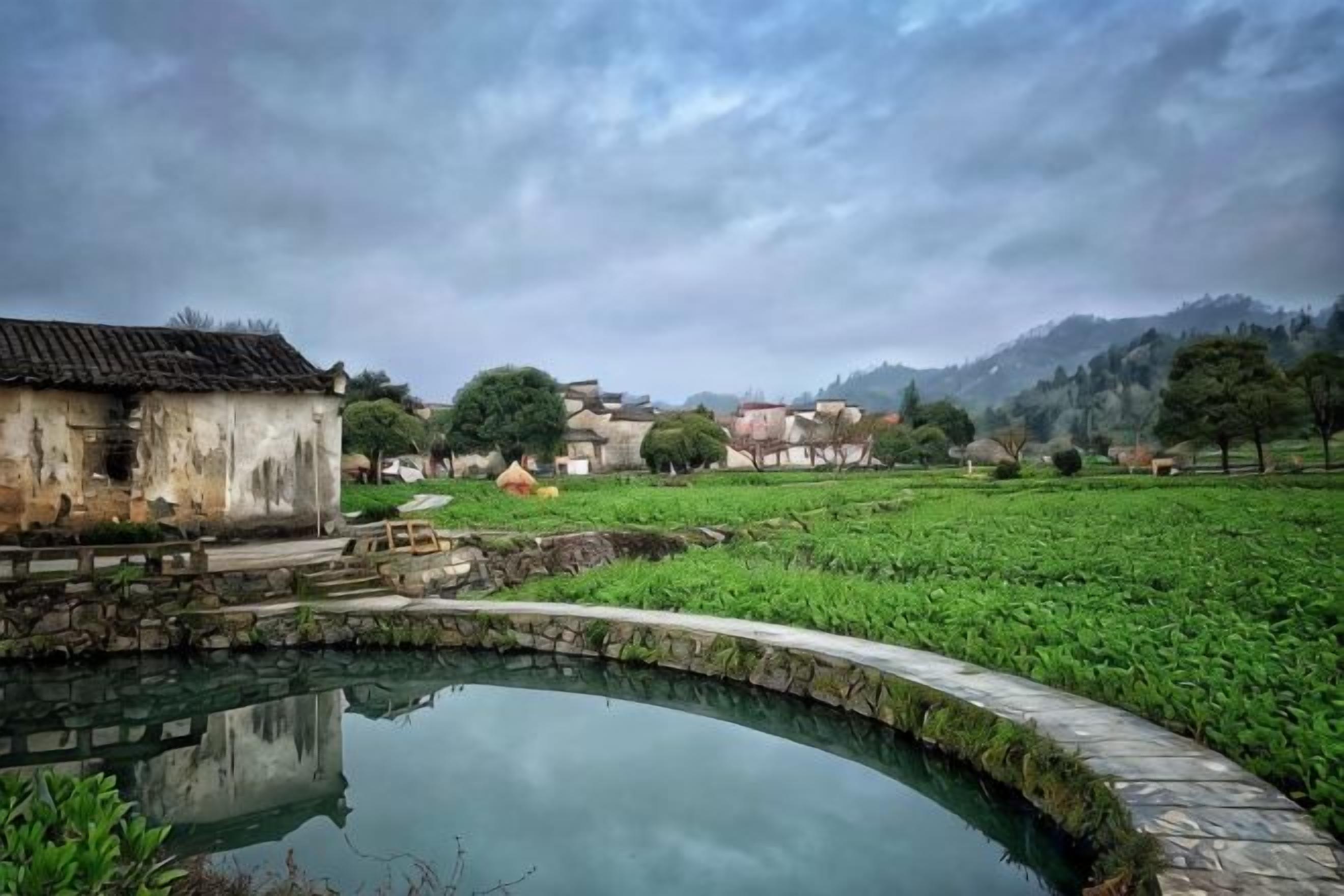 A traditional village with a pond, stone pathway, and rustic buildings.