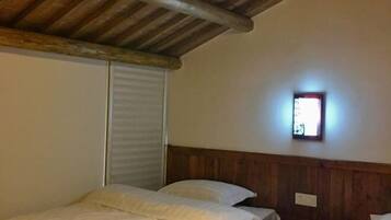 Una habitación con dos camas, vigas de madera en el techo, una ventana pequeña con vistas y una lámpara fijada a la pared.
