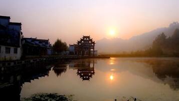 A traditional building with a reflection in a calm body of water, surrounded by a misty landscape.