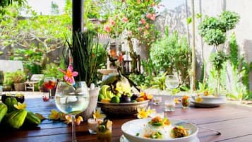 An outdoor dining area with a table set for a meal, surrounded by greenery and a decorative fountain.