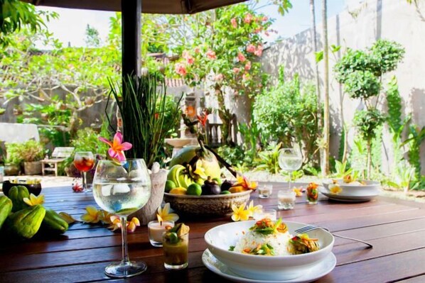 An outdoor dining area with a table set for a meal, surrounded by greenery and a decorative fountain. - Coliving Bali Sweet Home Tabanan,Daily & Monthly Stay,Kost Bulanan (Bali)