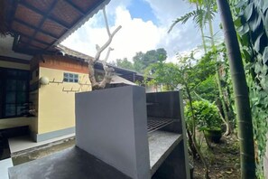 A courtyard with a concrete structure, a building with a tiled roof, and lush greenery. - Coliving Bali Sweet Home Tabanan,Daily & Monthly Stay,Kost Bulanan (Bali)