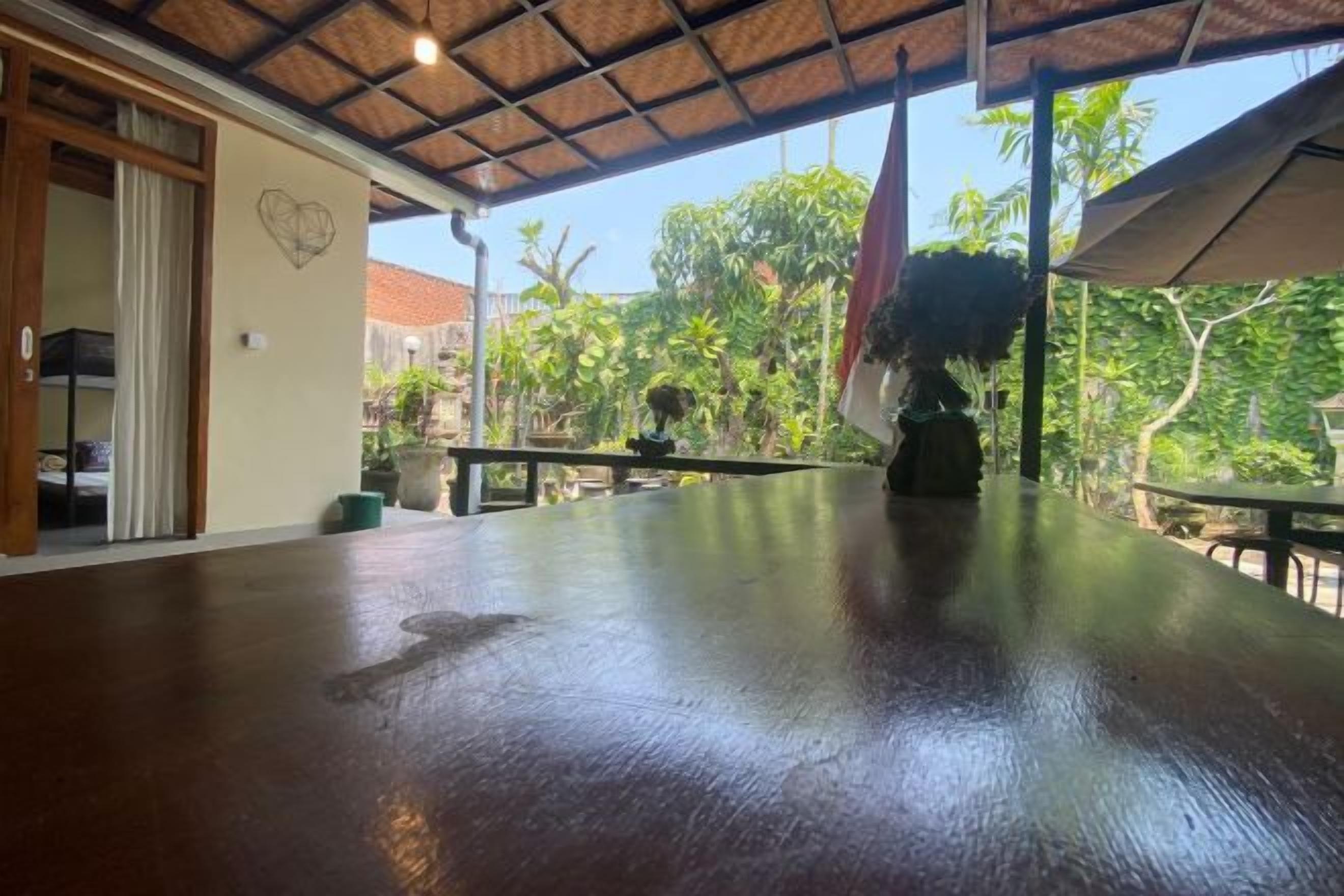 An indoor area with a wooden floor, a table, and a view of a garden with palm trees.