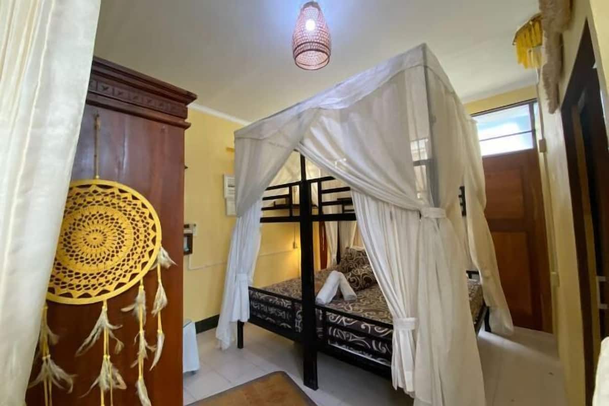 Un lit simple avec un baldaquin, un attrape-rêves et une suspension lumineuse dans une pièce dotée d’une armoire en bois et d’une porte.