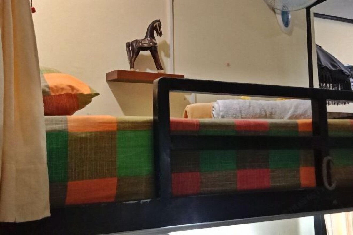 Un lit superposé avec une couverture à carreaux, une décoration en forme de cheval en bois et un ventilateur fixé au mur.