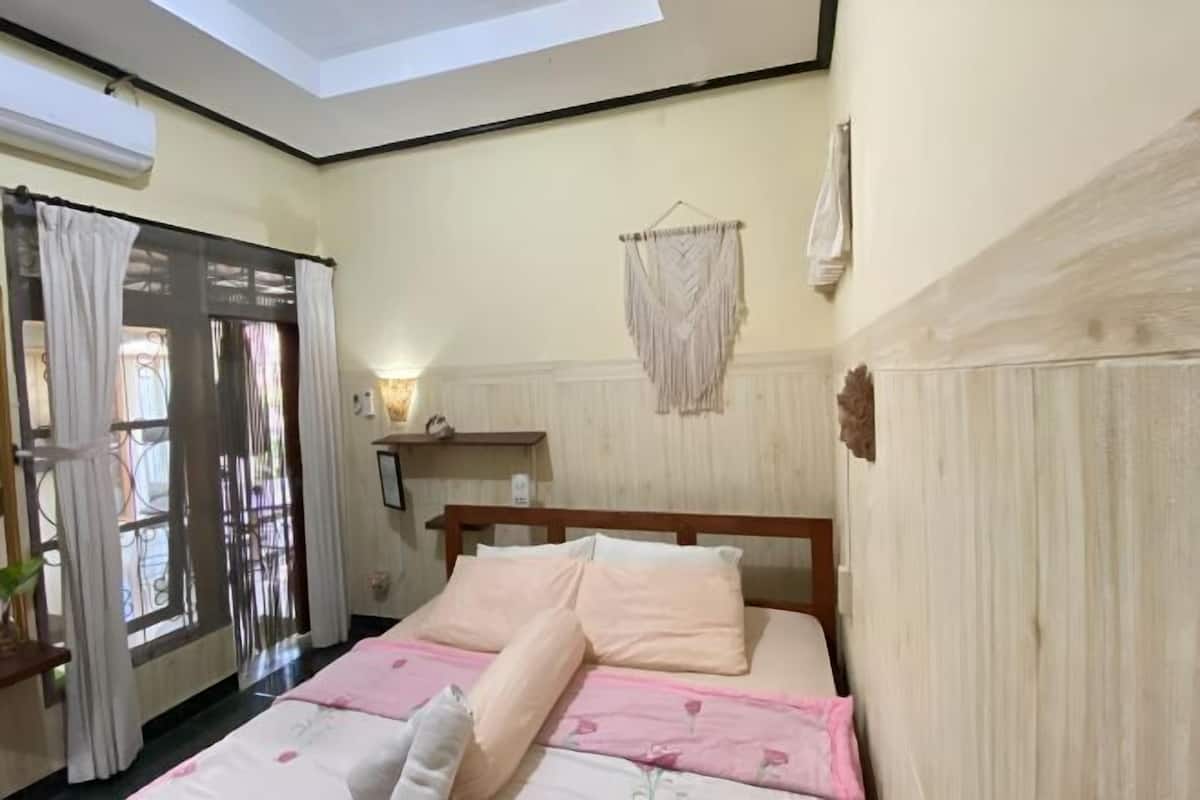 Une chambre à coucher avec un lit, une fenêtre avec des rideaux, un luminaire fixé au mur et un ventilateur de plafond.