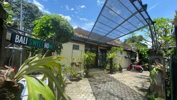 A courtyard with a sign that reads 'BALI SWEET HOME,' surrounded by potted plants and a red vehicle.