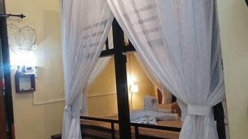 Una habitación con una cama bajo un dosel, una mesita de noche y una lámpara de pared.