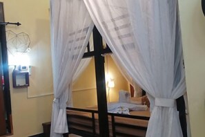 Une chambre avec un lit sous un dais, une table de chevet et une lampe fixée au mur.