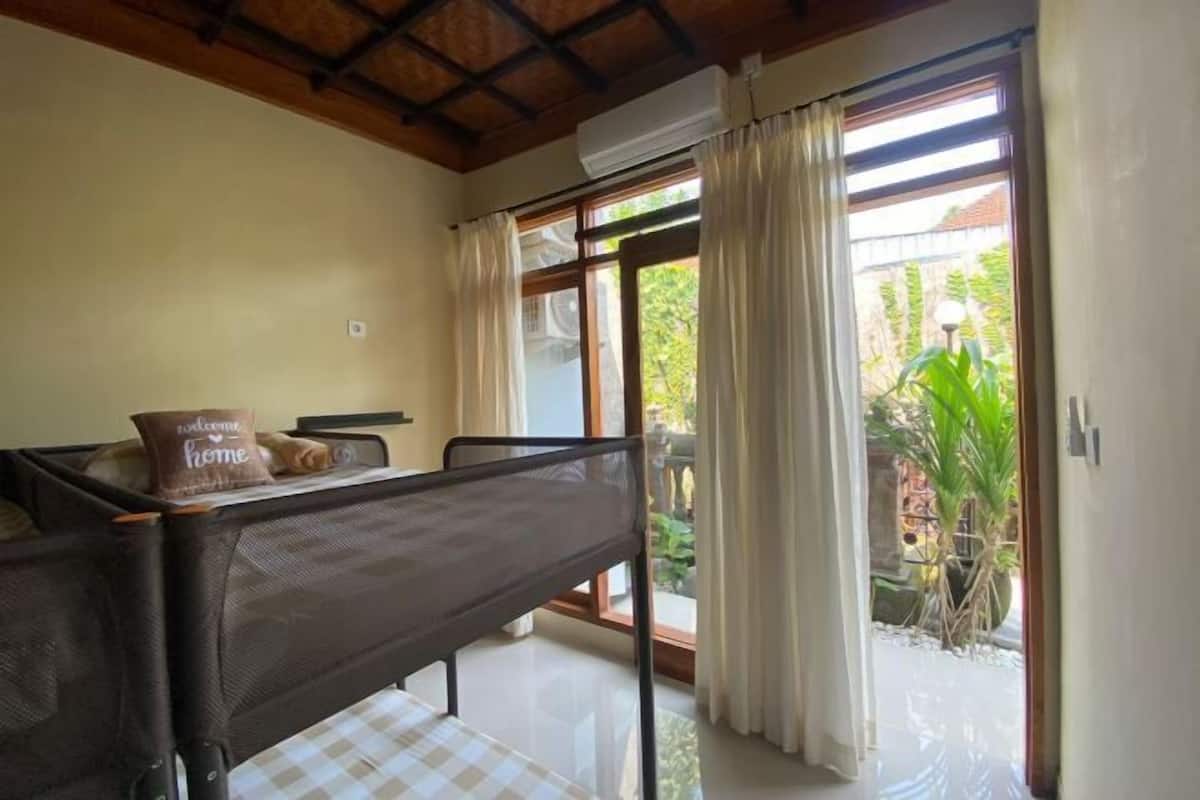 Une pièce avec un lit, un oreiller, une table et une fenêtre avec des rideaux.